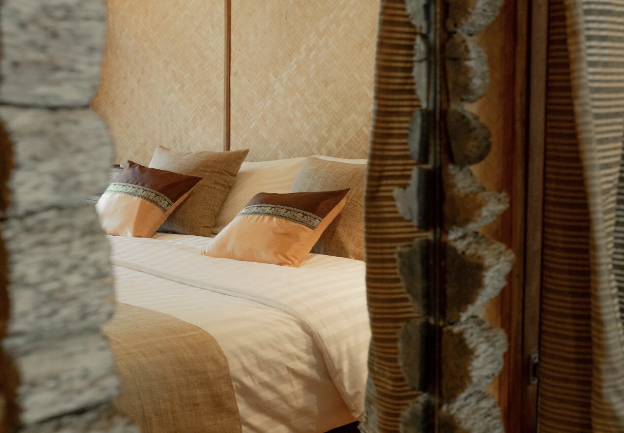 Close detail of a bungalow bed with a woven headboard and natural linens