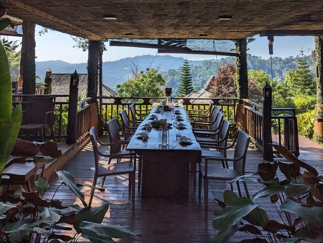 A long communal dining table on an open deck looking out over forested mountains