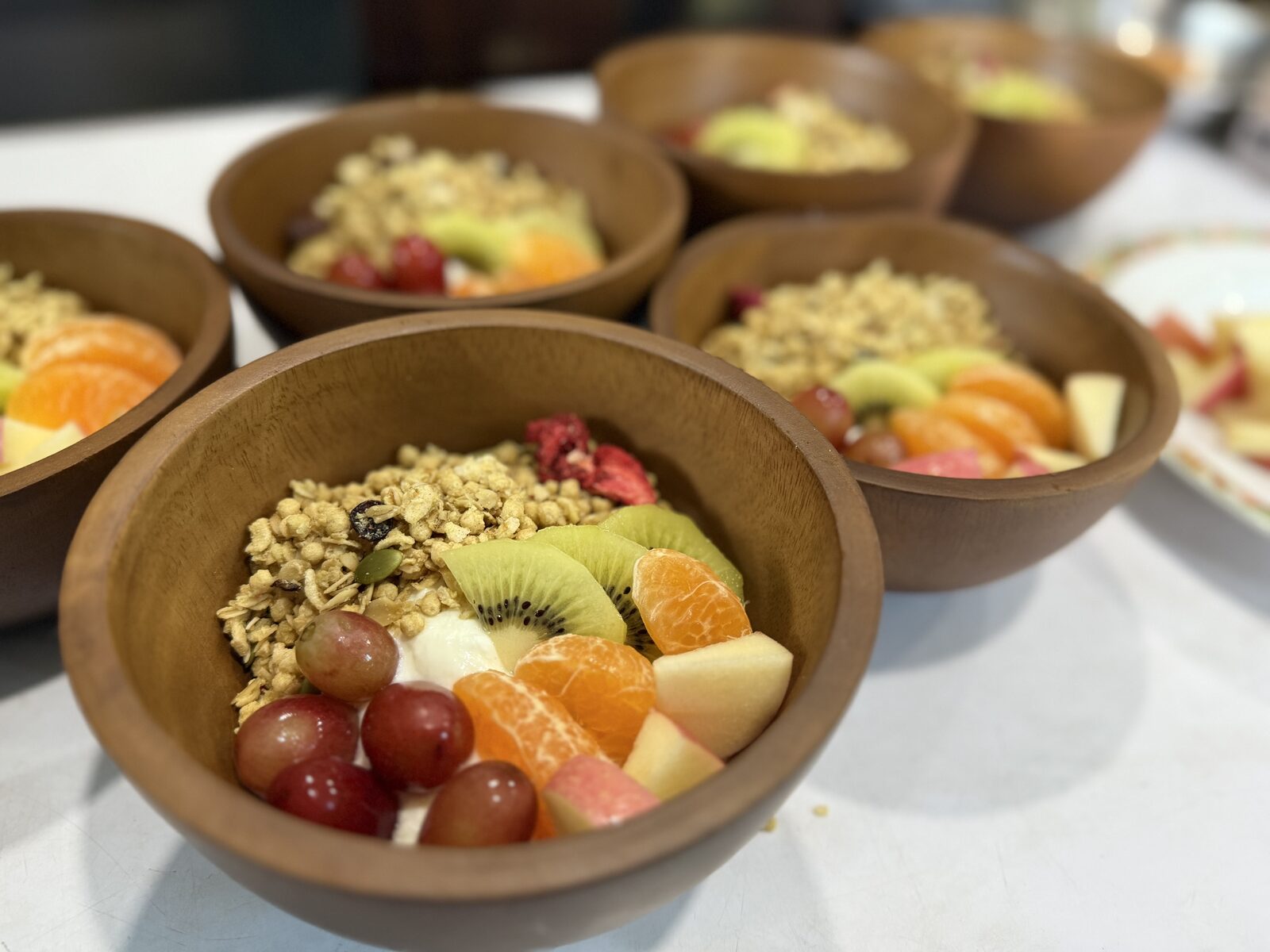 Wooden bowls of granola, yogurt and fresh cut fruit